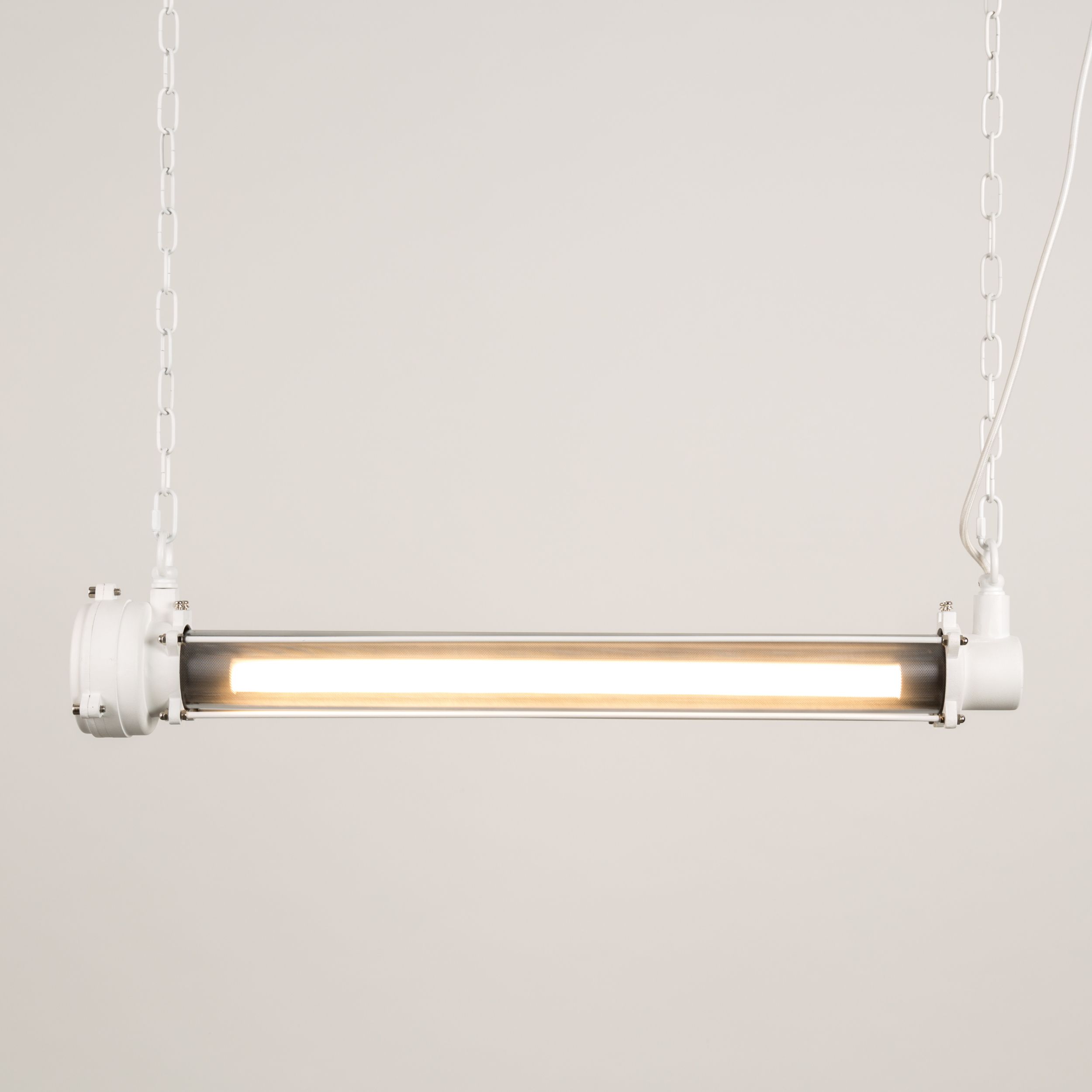Eingeschaltete weiße Röhren-Hängelampe mit hell leuchtender LED-Röhre und dekorativem Lochblech-Diffusor vor hellem Hintergrund.