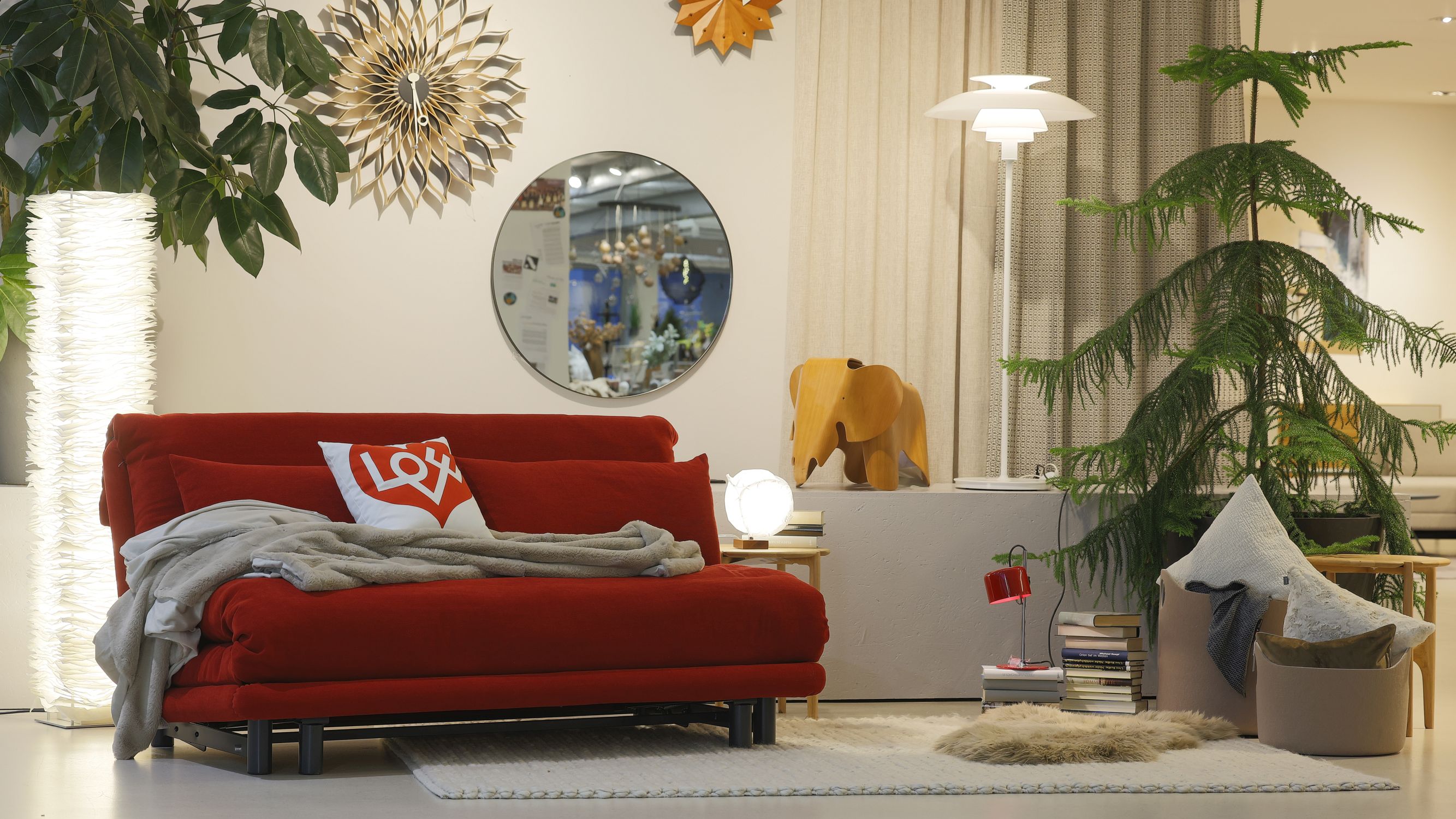 Rotes Schlafsofa Multy von Ligne Roset in einem Wohnraum mit Pflanzen und rundem Spiegel