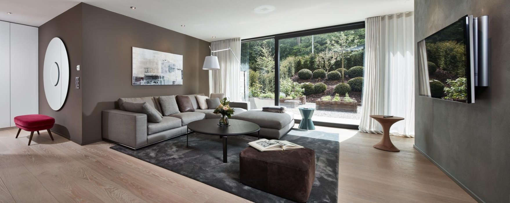 Wohnzimmer mit grauem Ecksofa, Fernseher und Terrassentüren