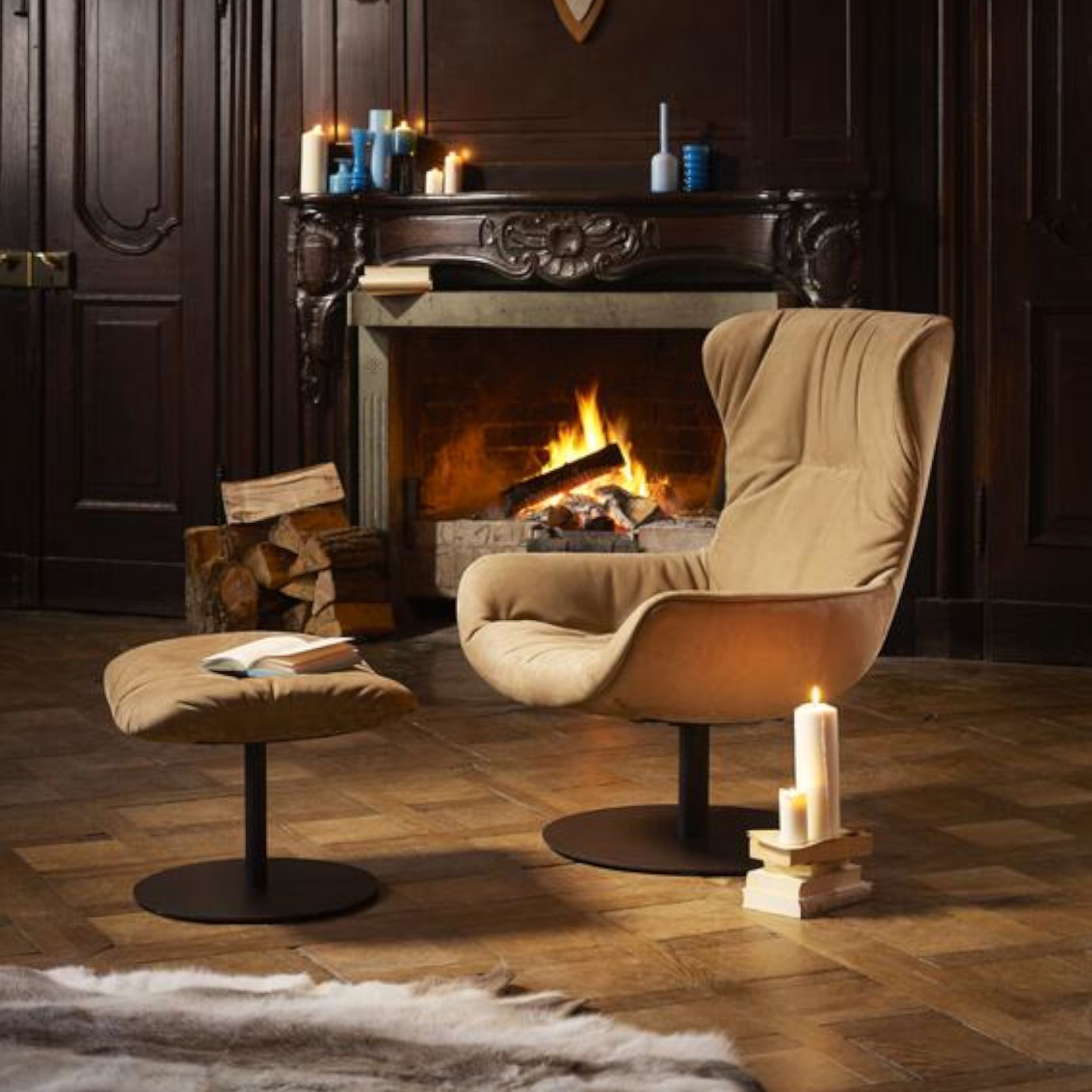 Das Bild zeigt ein gediegenes Kaminzimmer mit einem hellbraunen Sessel Leya Wingback Chair und passendem Hocker vor dem offenen Feuer.
