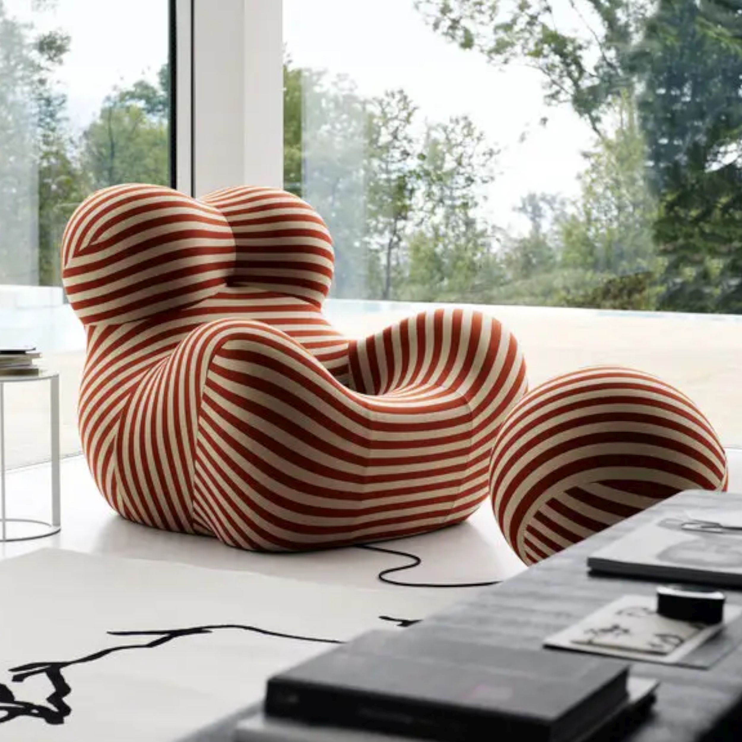 Orange-beige gestreifter Sessel Up von B&B Italia mit kugelförmigem Hocker in einem modernen Wohnraum vor einem großen Fenster.