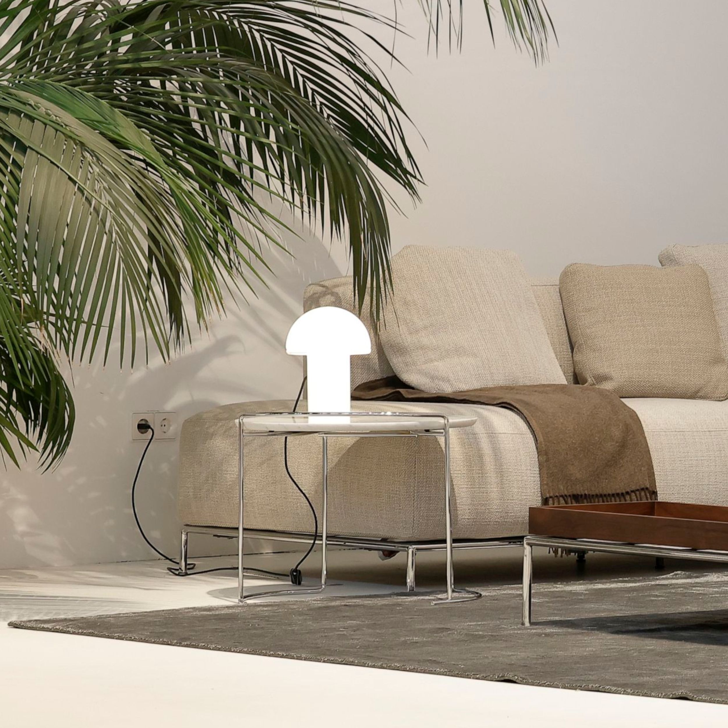 Ein gemütliches Wohnzimmer mit einem Stoffsofa und modernen Tischen und einer Pflanze in der Ecke. 
